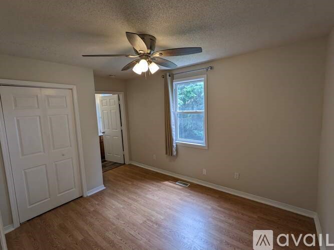 A room with a ceiling fan and a window with a view of trees outside.