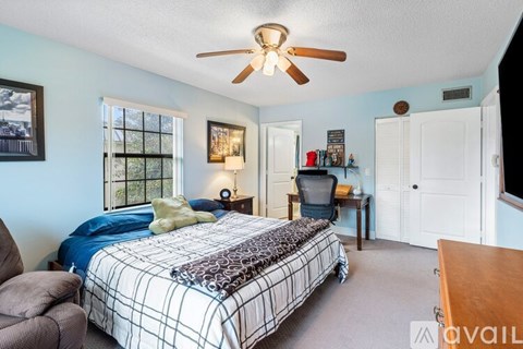 A bedroom with a bed, chair, and a ceiling fan.