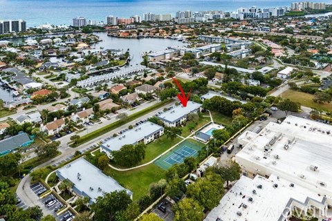An aerial view of a city with a red arrow pointing to a tennis court.