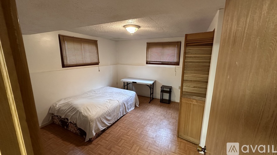 A bedroom with a bed, a small table, and a window with blinds.