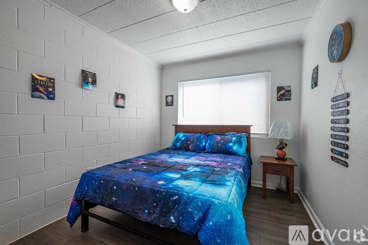A bedroom with a bed covered in a blue galaxy print bedspread.
