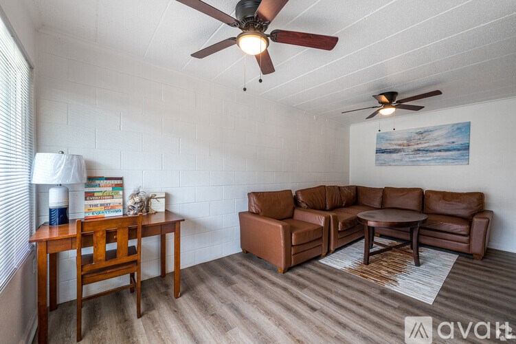 A living room with a brown leather couch, a wooden table, and a ceiling fan.