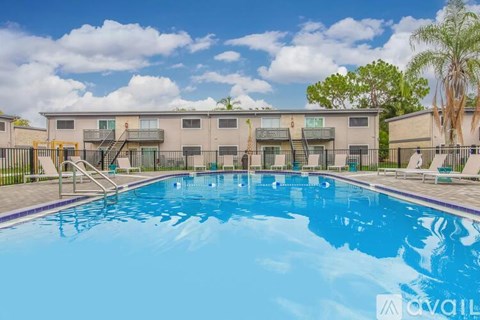 A pool surrounded by palm trees and lounge chairs in front of apartment buildings.
