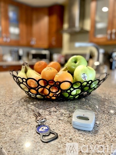 A bowl of fruit sits on a countertop with a keychain and a remote control nearby.