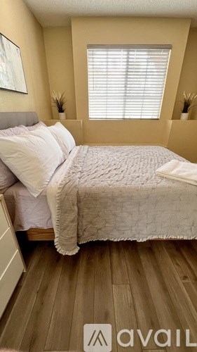 A bedroom with a bed, wooden floors, and a window with blinds.