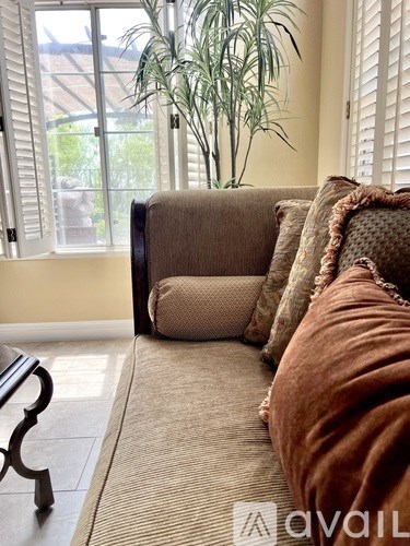 A sofa with pillows and a glass coffee table with a bowl of fruit on it.