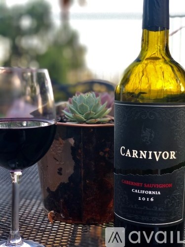 A bottle of Carnivor Cabernet Sauvignon 2016 wine is on a table next to a glass of wine.