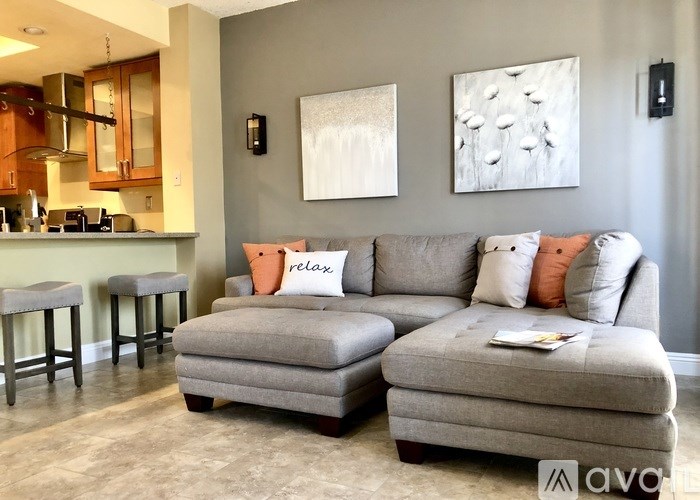 A living room with a grey couch and a kitchen area in the background.