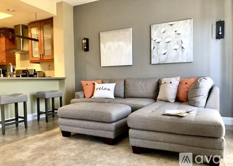 A living room with a grey couch and a kitchen area in the background.