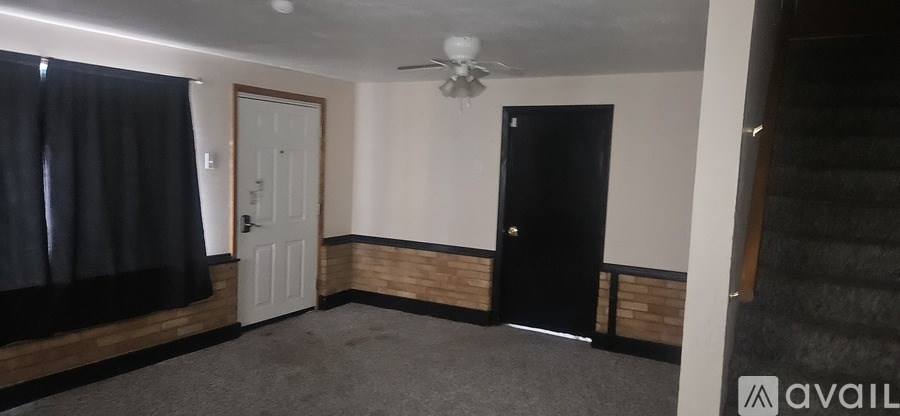 A room with a black door and a white door, a window with black curtains, and a wooden panel on the wall.