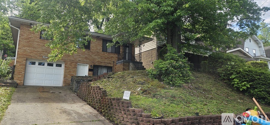 A house with a garage is surrounded by a brick wall and trees.