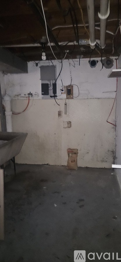 A dirty basement with a white wall and a brown pipe.