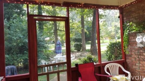 A red chair is in front of a window with a view of a lawn and trees.