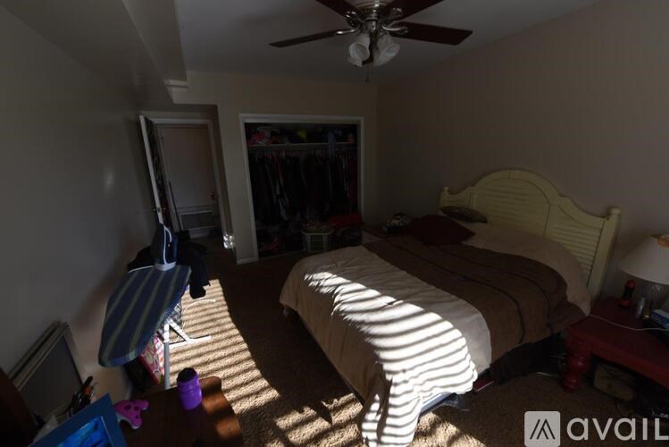 A bedroom with a bed, a ceiling fan, and a window with sunlight streaming in.