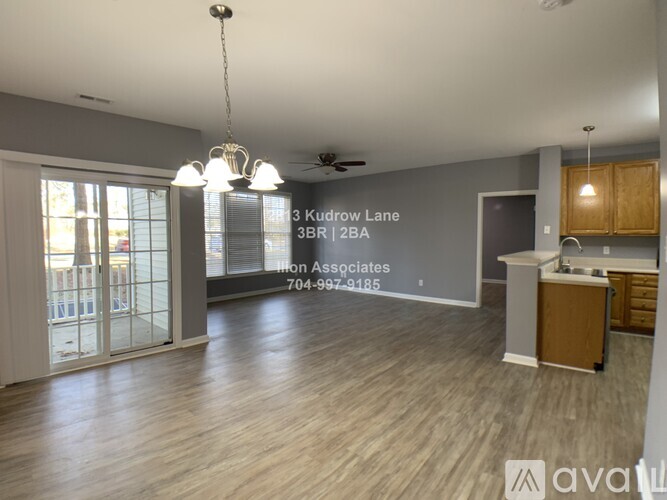 A spacious living room with a kitchen area and a sign that reads "13 Kudrow Lane 3BR 2BA Iron Associates 704-997-4185".