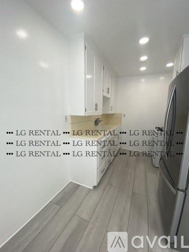 A kitchen with white cabinets and a refrigerator with the words LG RENTAL repeated on the wall.