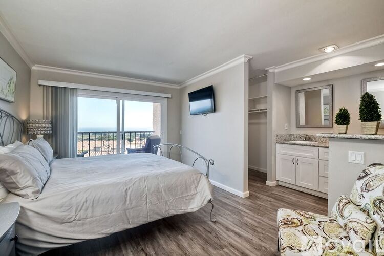 A bedroom with a large bed, a flat screen TV, and a window with a view of the outside.