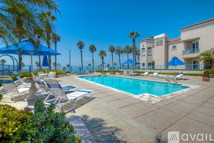 A pool surrounded by chairs and umbrellas with a building in the background.