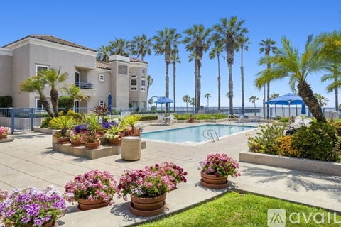 A pool surrounded by chairs and umbrellas with a building in the background.
