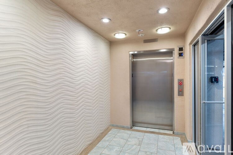 A stainless steel elevator is located in a hallway with a textured wall.