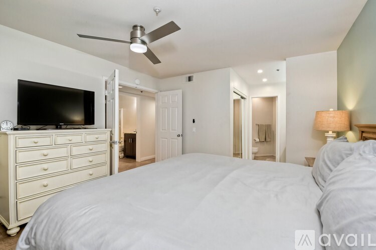 A bedroom with a large bed, a dresser with a flat screen TV, and a ceiling fan.