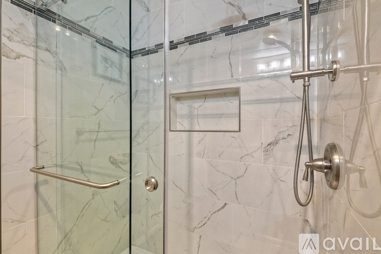 A shower area with a glass door and a marble wall.