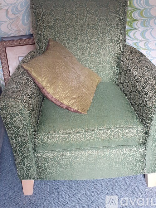 A green patterned chair with a gold pillow on it.
