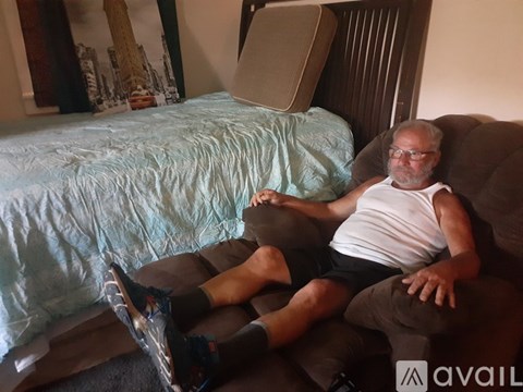 A man in a white tank top and black shorts is sitting on a brown couch.