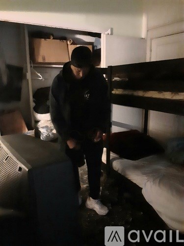 A person in a black hoodie is standing in a room with a bunk bed and a television.