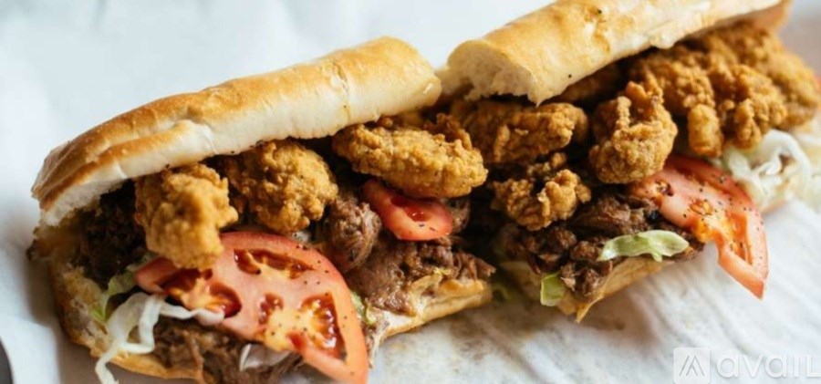 A sandwich with fried chicken, beef, lettuce, and tomato slices.