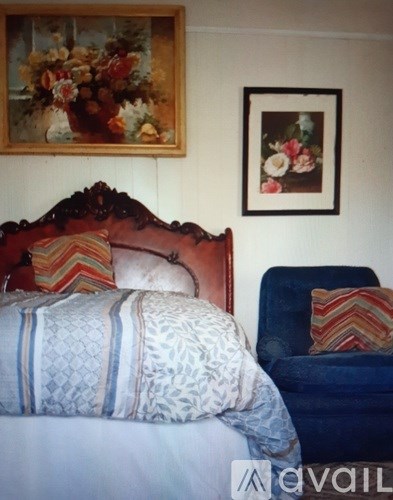 A bed with a blue and white comforter and a red headboard sits next to a blue chair with a striped pillow.