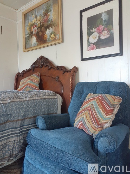 A blue chair with a striped pillow is in front of a bed with a striped blanket.