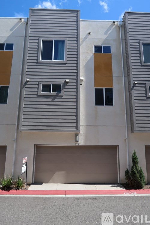 A modern building with a grey facade and a red stripe at the base.