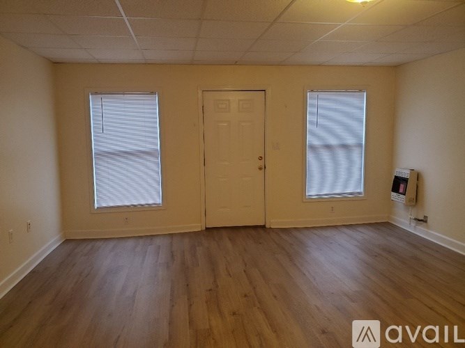 A room with wooden floors and two windows with blinds.