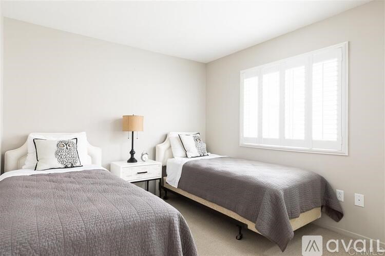 Two beds with grey bedspreads in a room with white walls.