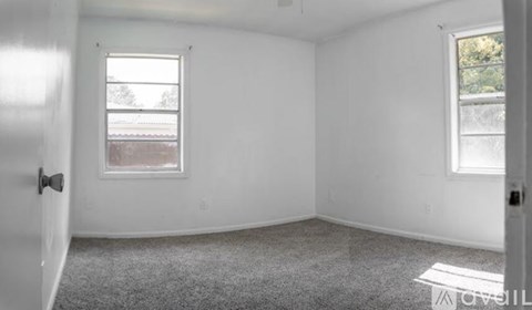 A room with a carpeted floor, two windows, and a door.