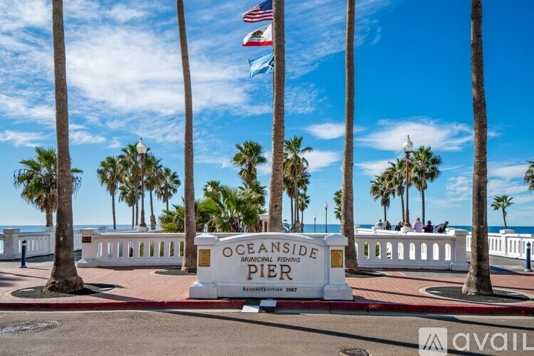 A sign that says Oceanside Pier stands in front of palm trees.
