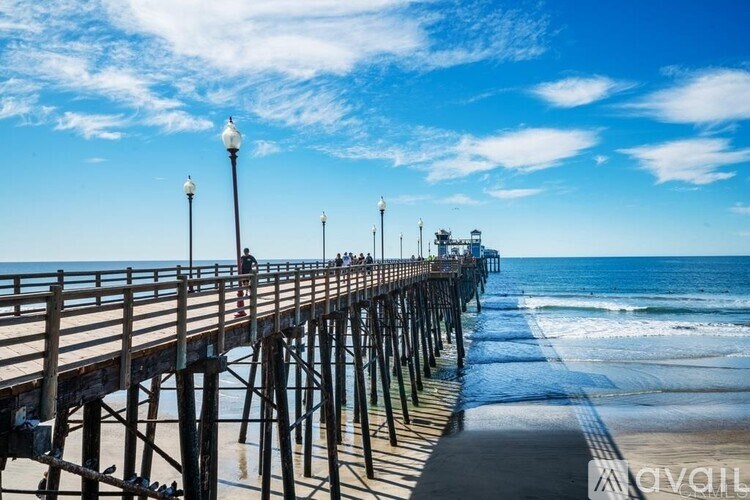 A long wooden pier with people walking on it and a lighthouse in the distance.