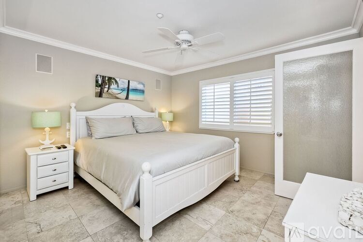 A bedroom with a white bed, nightstand, and a ceiling fan.