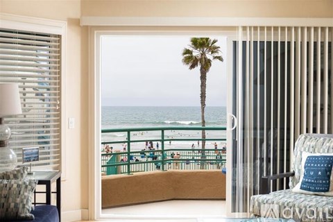 A view of a beach from a room with a chair and a table.