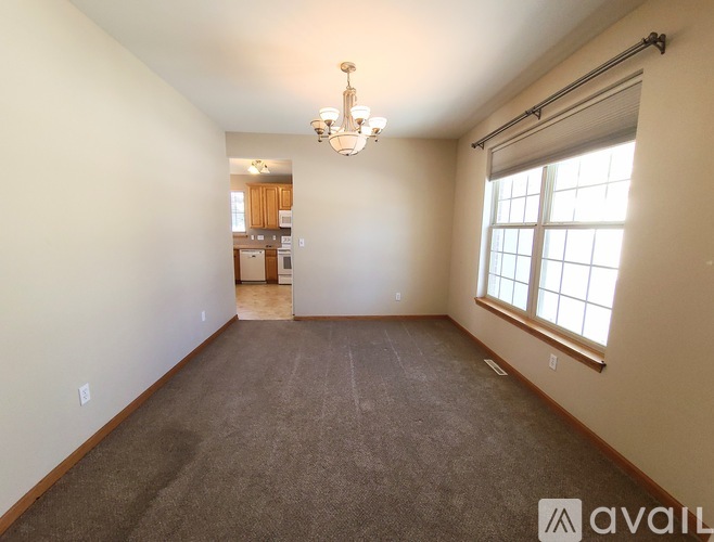 A spacious room with a carpeted floor, a chandelier, and a window with blinds.