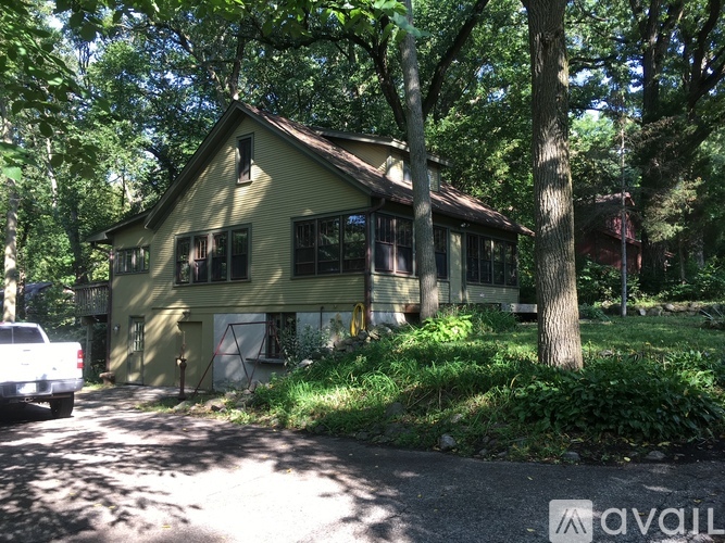 A house with a green exterior is surrounded by trees and has a white car parked in front.
