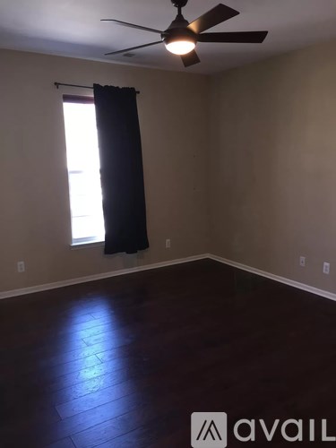 A room with a fan and a window with a black curtain.