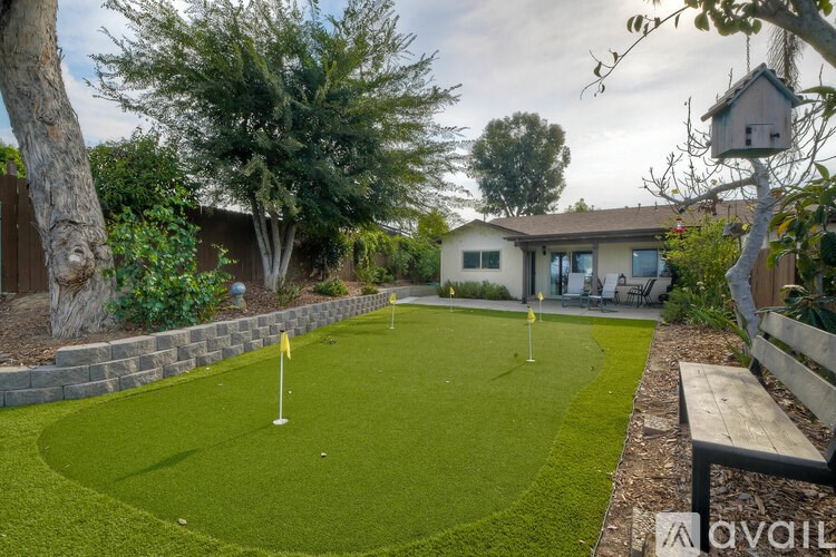 A backyard with a putting green and a house in the background.