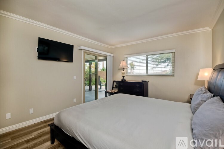 A bedroom with a large bed, a flat screen TV, and a sliding glass door leading to a balcony.