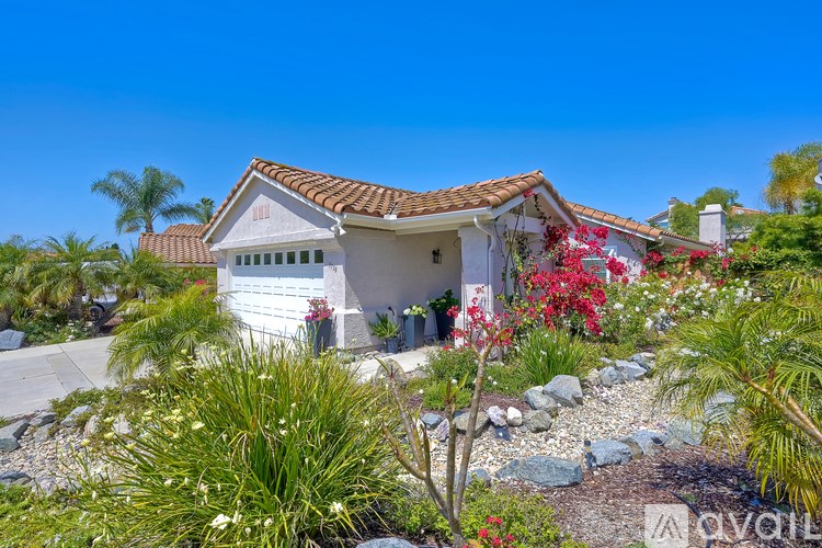A white house with a red tile roof surrounded by green plants and trees.