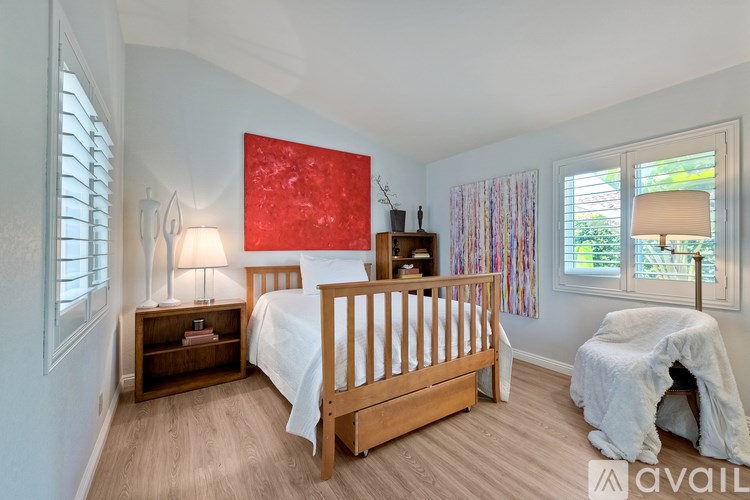 A bedroom with a large bed, a nightstand with a lamp, and a window with a view of trees.