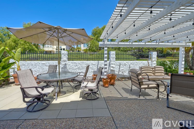 A patio with chairs and a table under a white pergola.