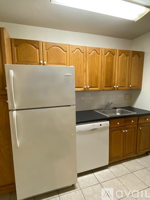A white refrigerator stands in a kitchen with wooden cabinets.