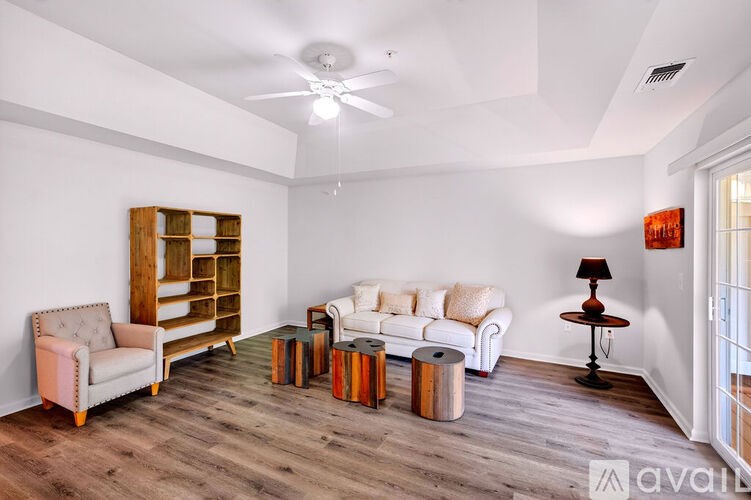 A living room with a white couch, a wooden bookshelf, a chair, a table with a lamp, and a ceiling fan.